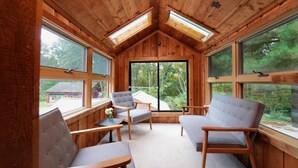 A cozy cabin interior with wooden walls, large windows, and a central seating area with two chairs and a table.