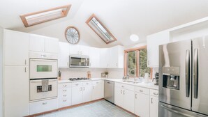 A modern kitchen with white cabinets, stainless steel appliances, and a skylight.