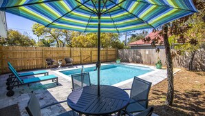 A backyard with a swimming pool, a patio table with chairs, and a striped umbrella. - New to Dune Allen Realty! 10-min walk or 2-minute golf cart ride away to beach! (Santa Rosa Beach)