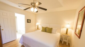 A bedroom with a large bed, two bedside tables with lamps, a ceiling fan, and a door leading to another room. - New to Dune Allen Realty! 10-min walk or 2-minute golf cart ride away to beach! (Santa Rosa Beach)