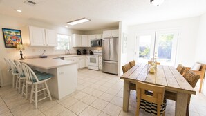 A modern kitchen with white cabinets, stainless steel appliances, and a wooden dining table with chairs. - New to Dune Allen Realty! 10-min walk or 2-minute golf cart ride away to beach! (Santa Rosa Beach)
