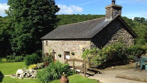 A stone cottage with a sloped roof, a wooden gate, and a grassy garden with potted plants. - The Mill House at Cwmiar Farm - Relaxing Holidays (Llanybydder)