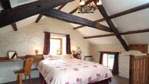 A bedroom with a sloped ceiling, a bed with a floral bedspread, a wooden chair, and a desk with a lamp. - The Mill House at Cwmiar Farm - Relaxing Holidays (Llanybydder)