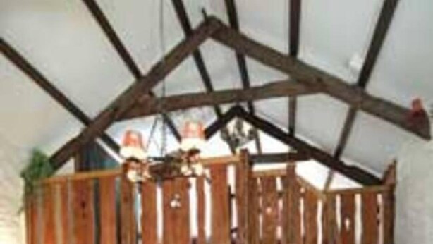 A rustic cabin interior with a loft bedroom, wooden beams, a dining area, and a staircase. - The Mill House at Cwmiar Farm - Relaxing Holidays (Llanybydder)