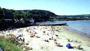 A beach with people sunbathing and swimming. There are tents and a pier extending into the water. - The Mill House at Cwmiar Farm - Relaxing Holidays (Llanybydder)