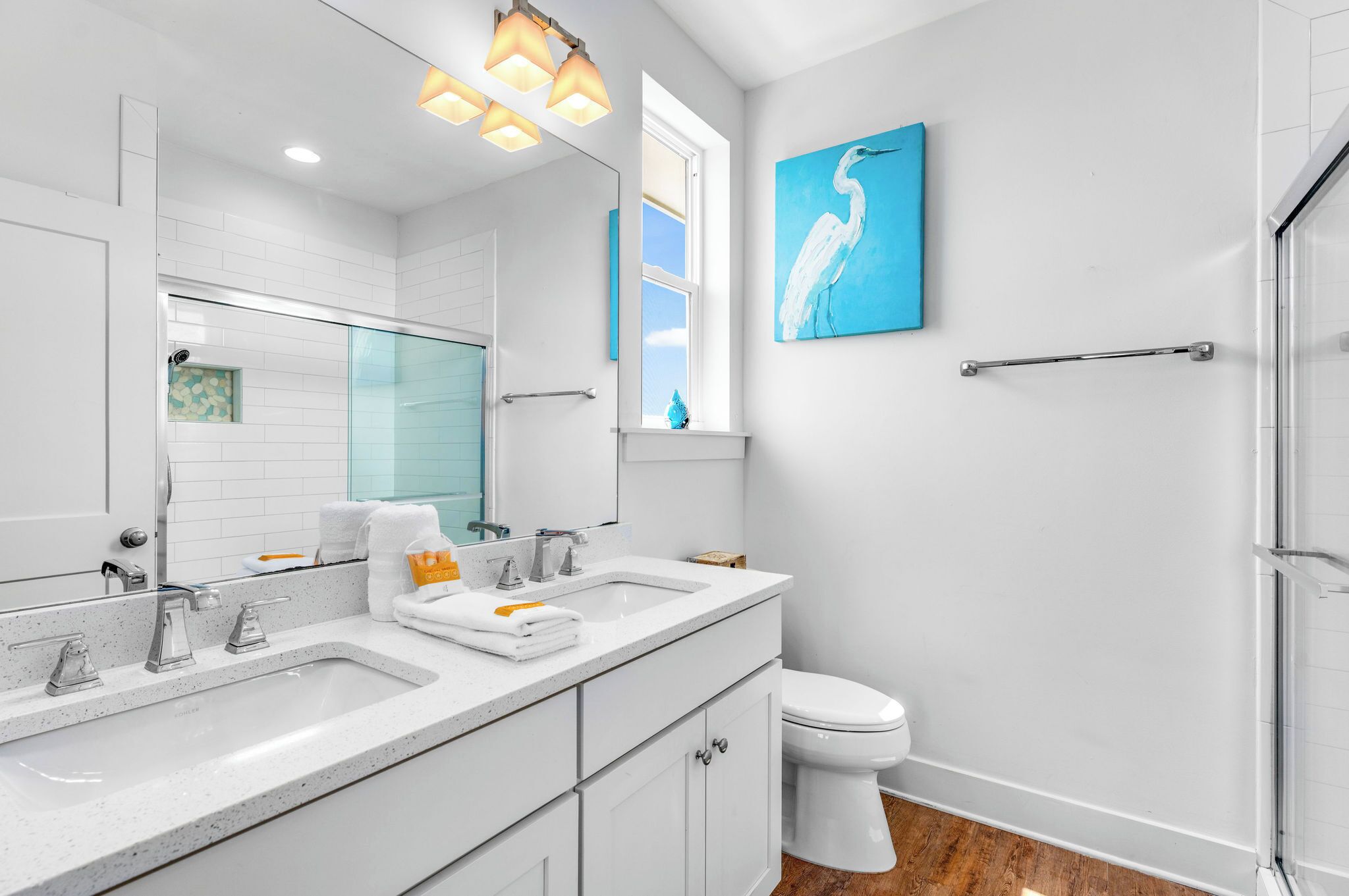 A modern bathroom with a large mirror, two sinks, a toilet, and a shower.