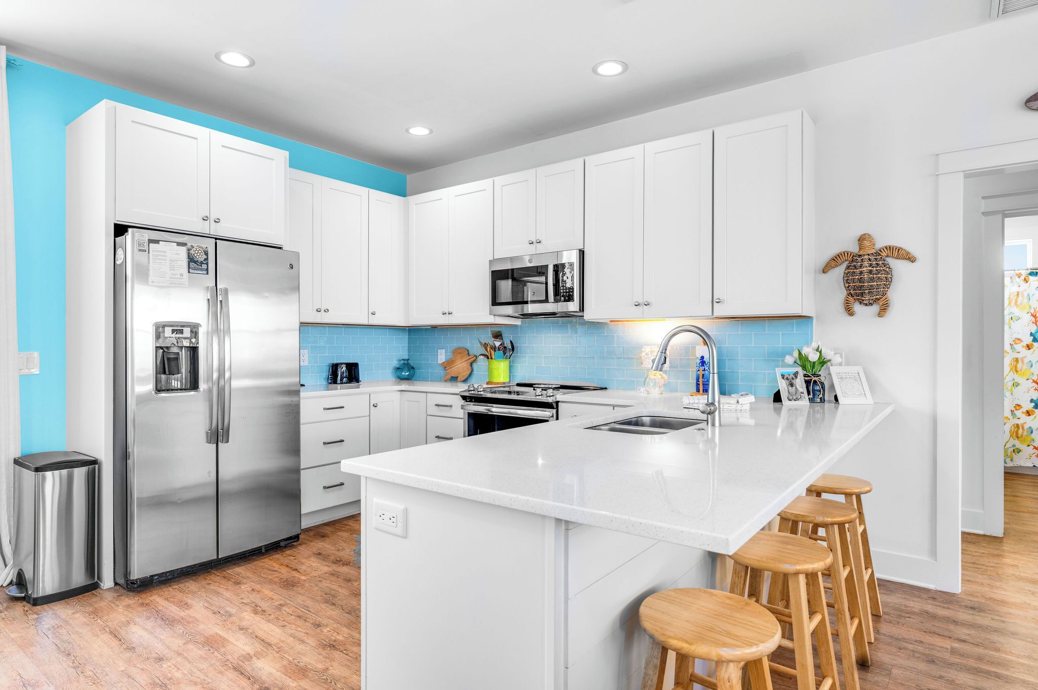 Una cocina moderna con armarios blancos, electrodomésticos de acero inoxidable, una isla central con taburetes y una pared azul de acento.