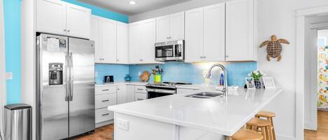 Una cocina moderna con armarios blancos, electrodomésticos de acero inoxidable, una isla central con taburetes y una pared azul de acento.