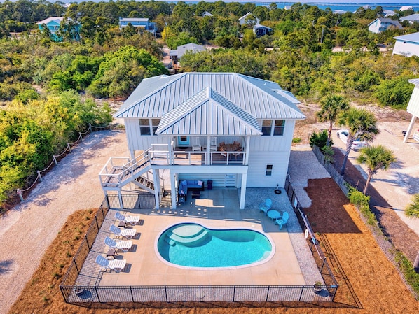 Una casa a due piani con piscina, circondata da alberi e vista sull'oceano.