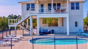 Une maison à deux étages avec un balcon, une piscine et du mobilier d’extérieur.