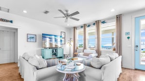 Un salon doté d’un ventilateur de plafond, d’un téléviseur, d’une table basse et offrant une vue sur l’océan.