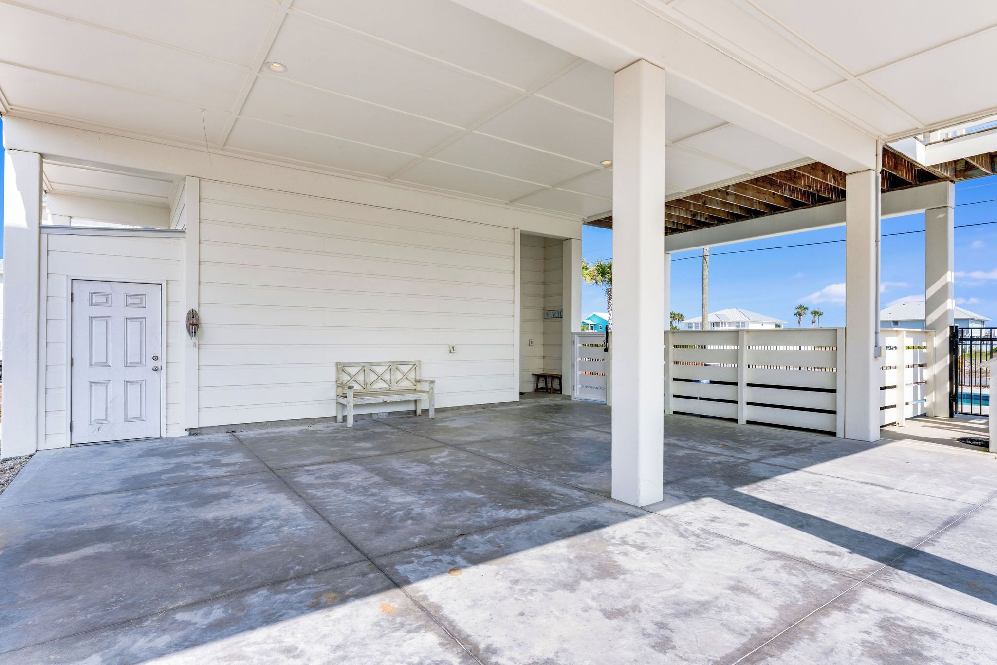 A covered outdoor area with a bench, a white door, and a fence.
