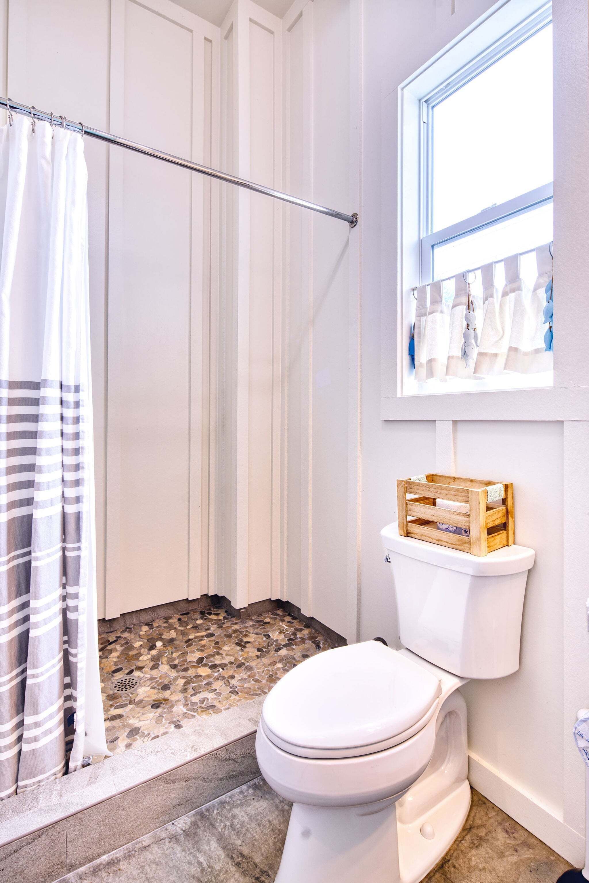 A bathroom with a shower, toilet, and a window above the toilet.