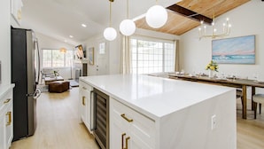 Una cocina moderna con una isla grande, luces colgantes y un comedor con vista al océano.