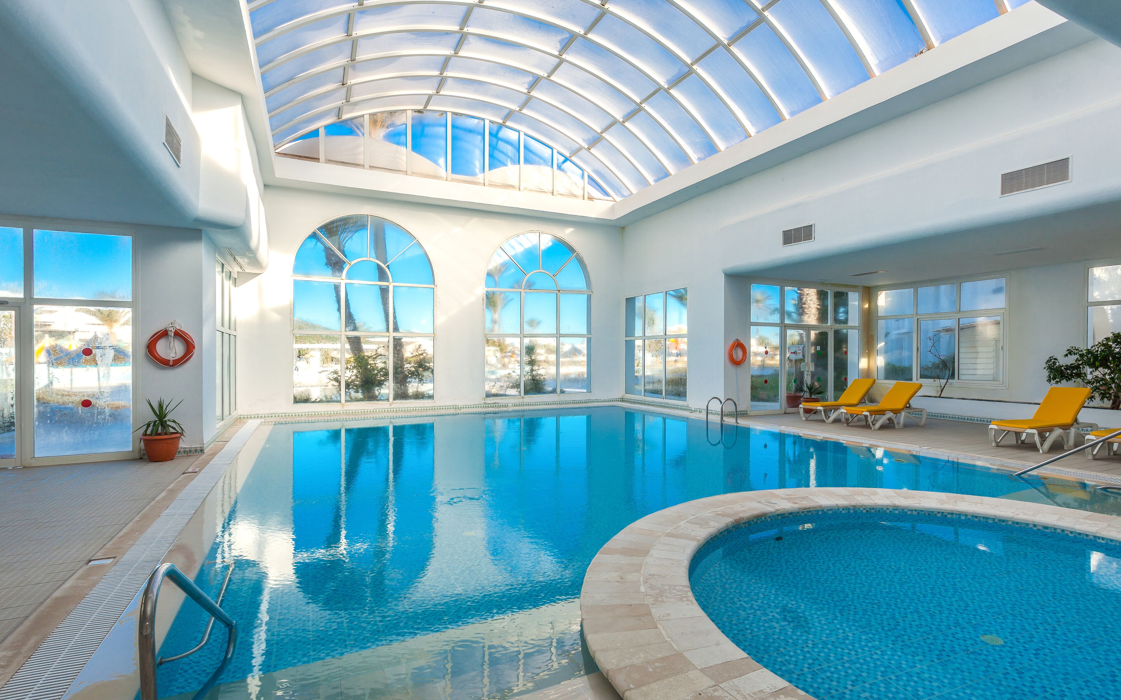 Ein Hallenbad mit klaren Glasdecken, Liegestühlen und einem Rettungsring an der Wand.
