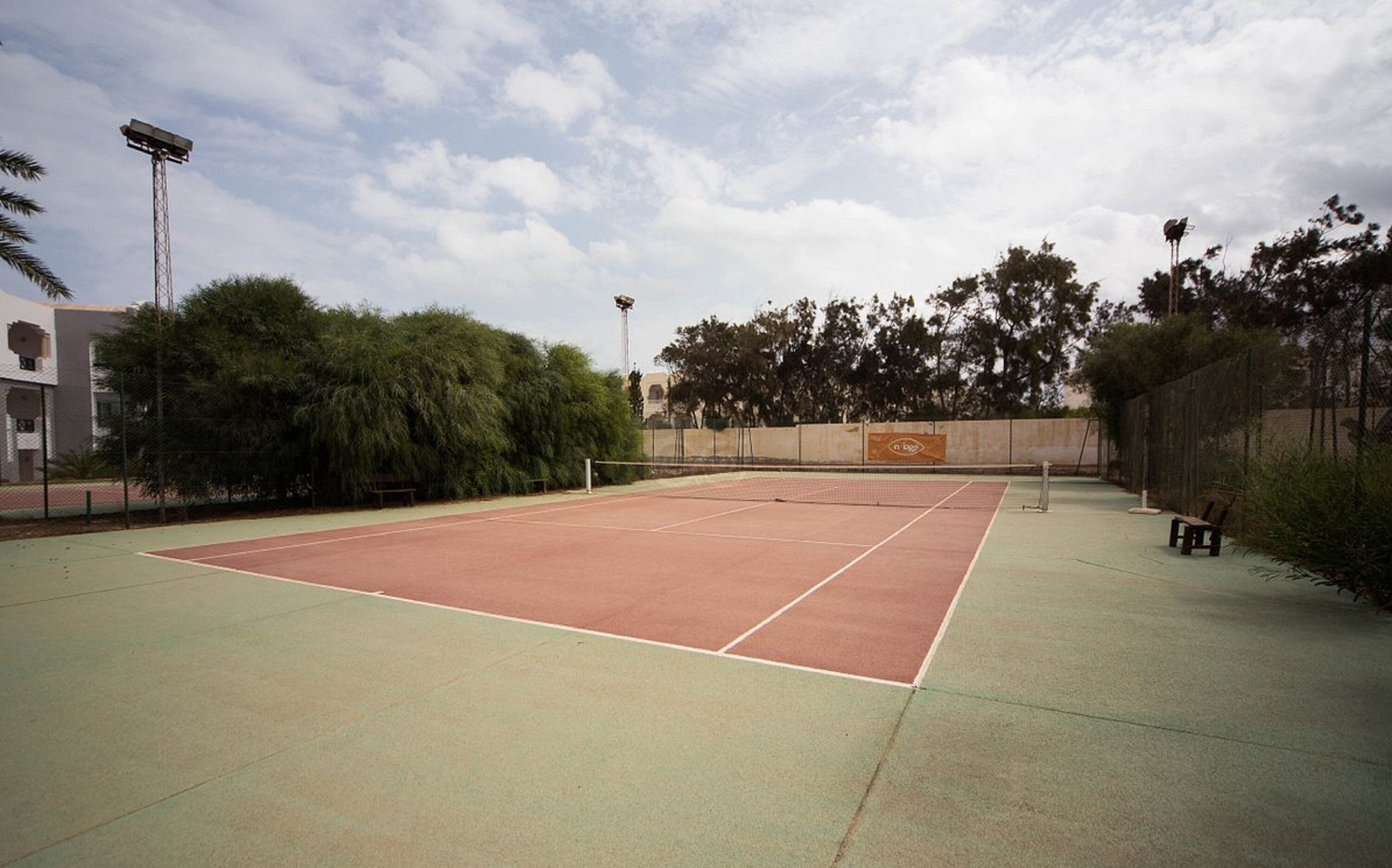 An outdoor tennis court with a net, surrounded by trees and a fence.