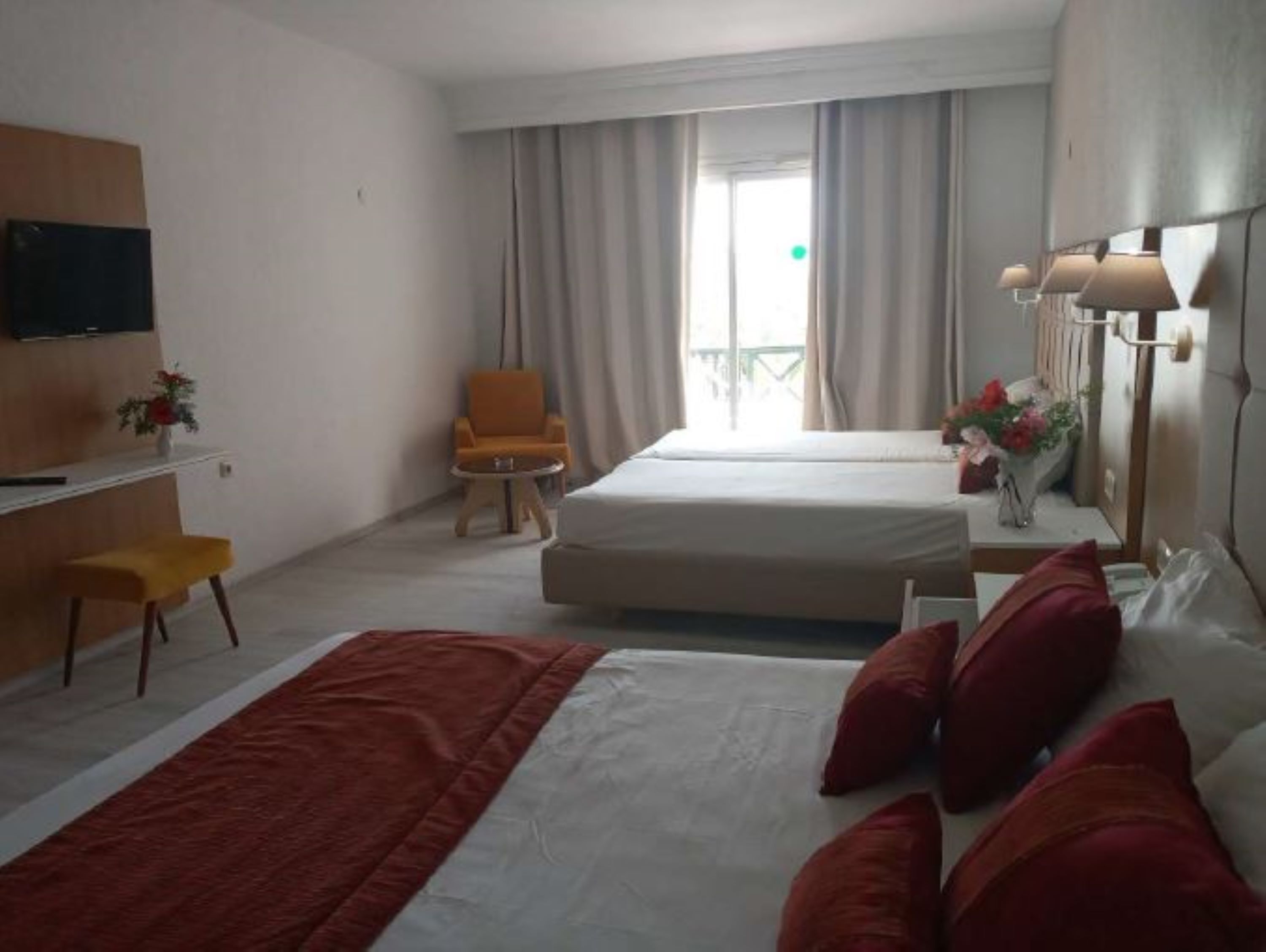 A hotel room with two beds, a desk, a chair, a TV, and a window with curtains.