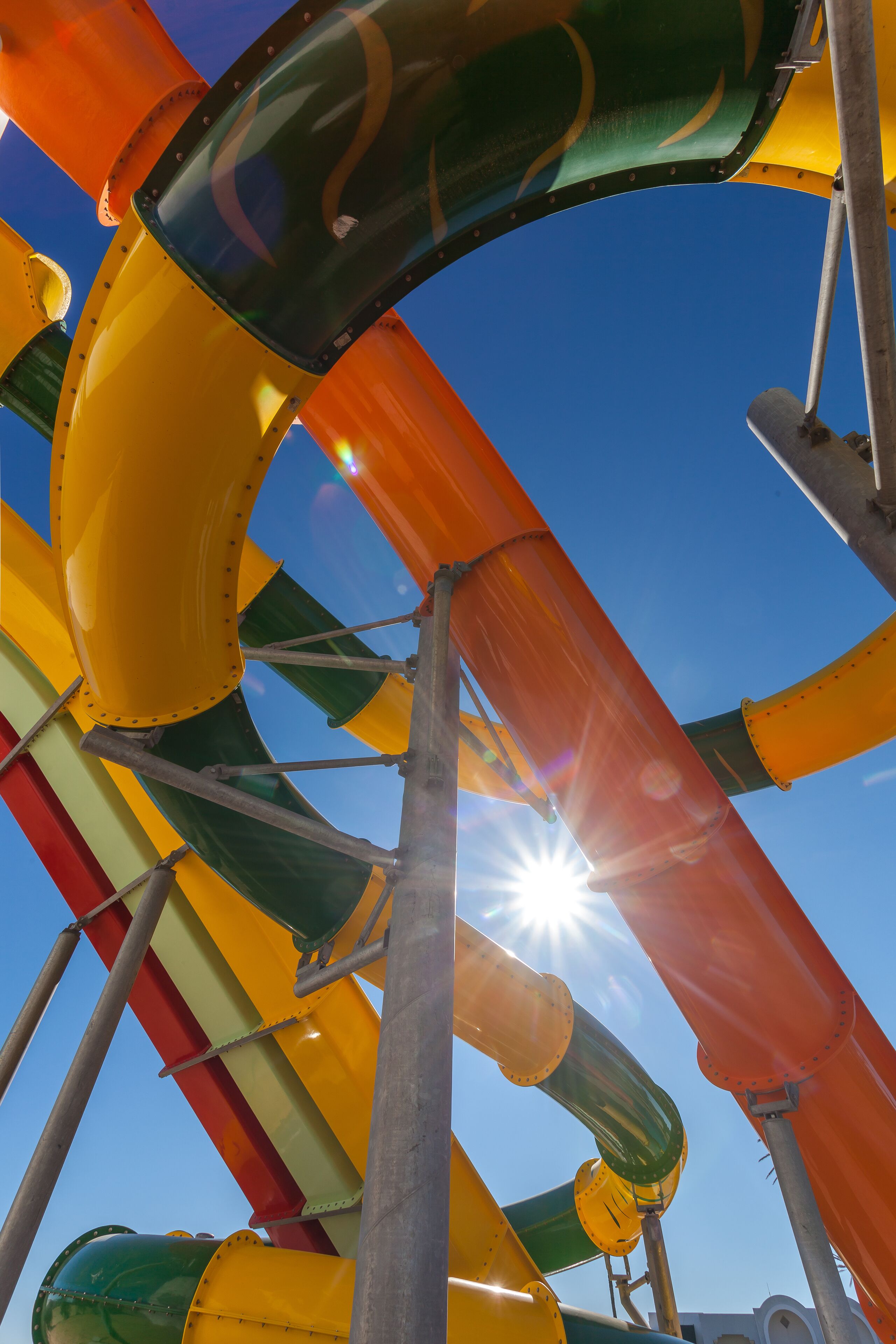 A water slide structure with multiple lanes, supported by metal beams, under a clear blue sky.