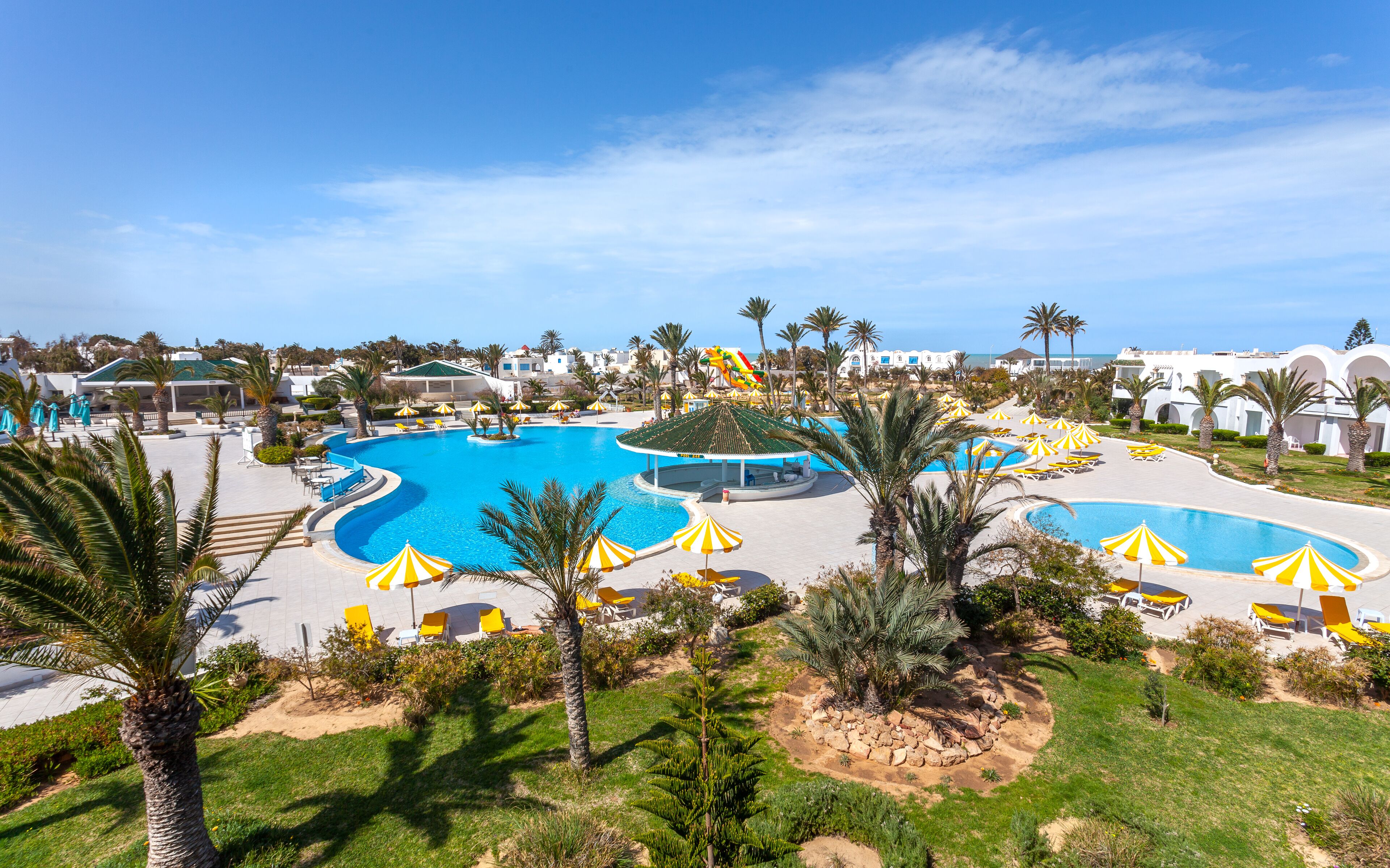 Un resort con varias piscinas, palmeras y tumbonas.