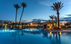 A resort pool area with palm trees, a bridge, and buildings with arched windows. - Djerba Holiday Beach (Mezraia)