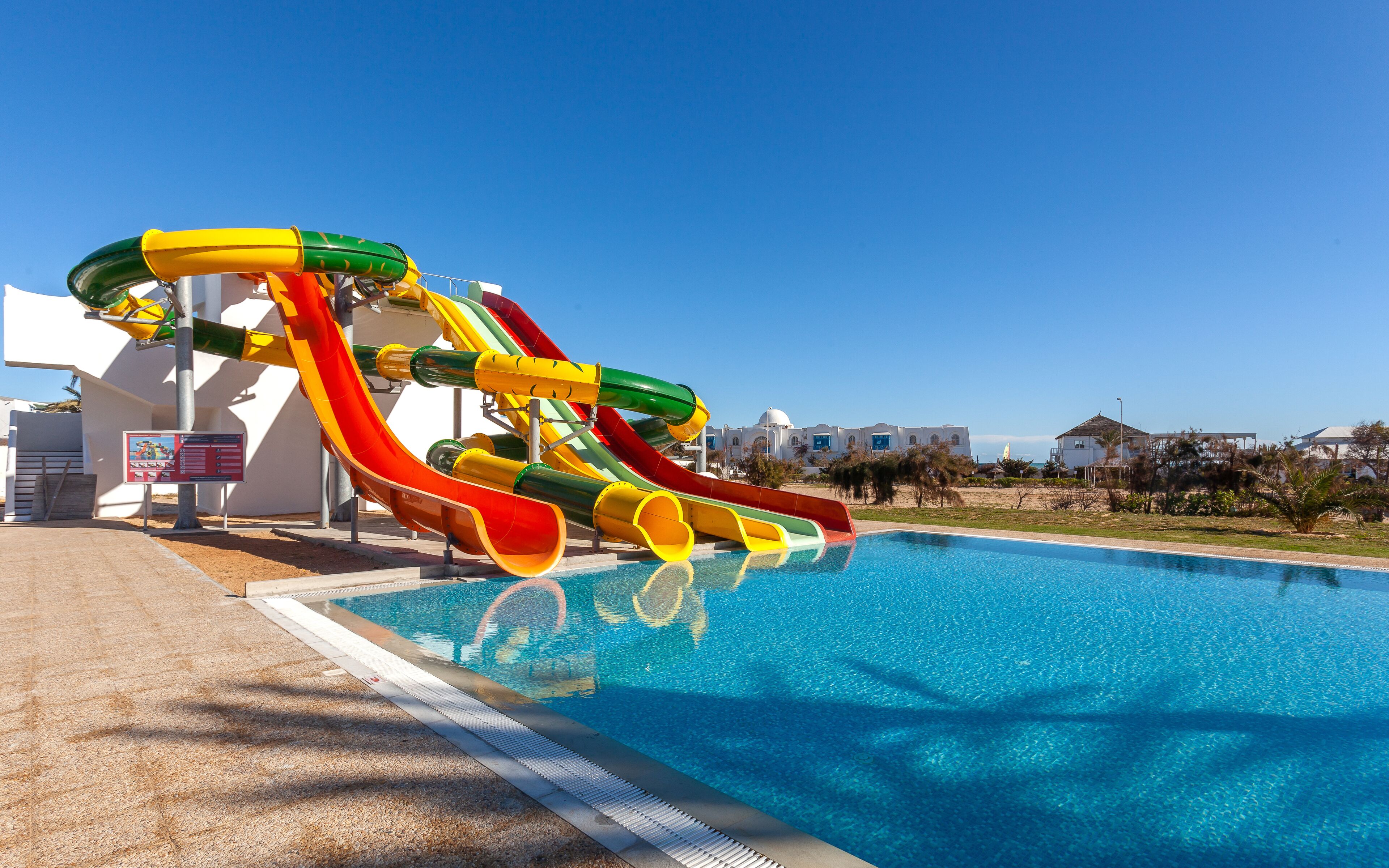 A swimming pool with a multi-colored water slide and a clear blue sky.