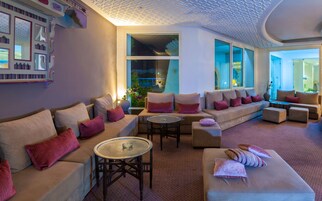 Una sala de estar moderna con varias zonas de estar, incluyendo sofás y una mesa redonda, con ventanas amplias que ofrecen luz natural y vistas.