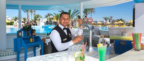 Zona de bar con vista a la piscina, con taburetes y un barman preparando una bebida.