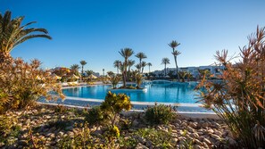 A pool surrounded by palm trees and rocks, with a clear blue sky in the background. - Djerba Holiday Beach (Mezraia)