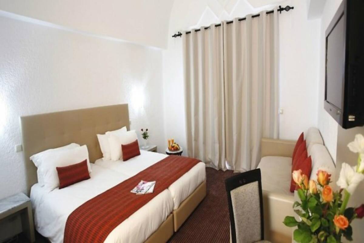 Ein Hotelzimmer mit einem Bett, einem Sessel, einem Fernseher und einem Vorhangfenster.