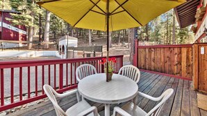 Une terrasse en bois avec une table ronde et quatre chaises, un parasol jaune et une rambarde rouge.