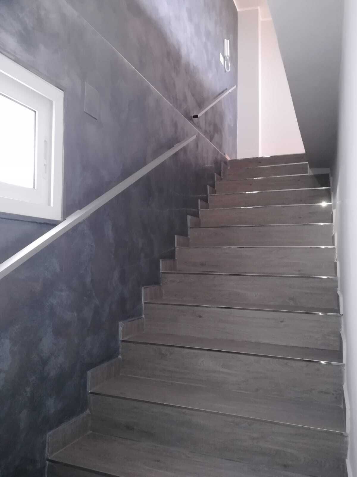 A staircase with dark grey steps and a white handrail, leading to a landing with a white door.