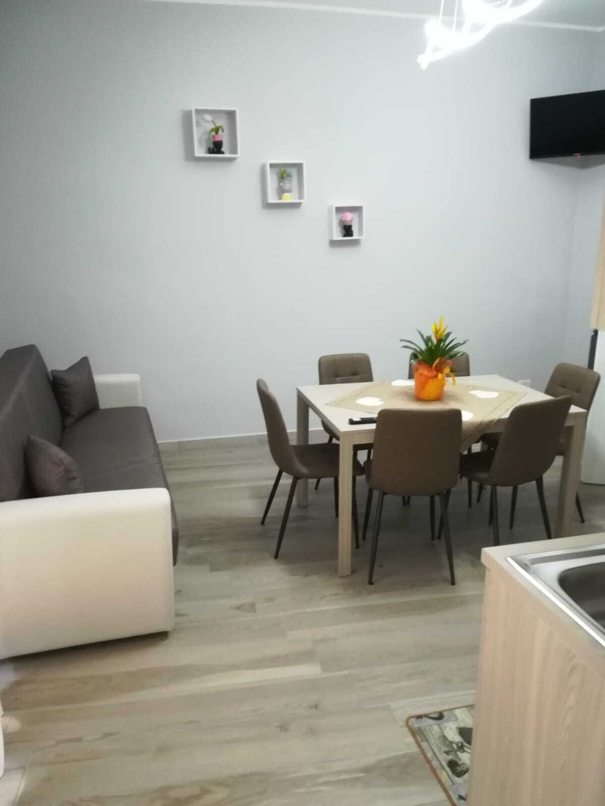 Un salon moderne avec un canapé gris, une table à manger avec des chaises et un petit coin cuisine équipé d’un évier.