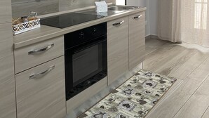 Une cuisine moderne avec des meubles de couleur bois clair, une plaque de cuisson noire et un tapis à motifs.