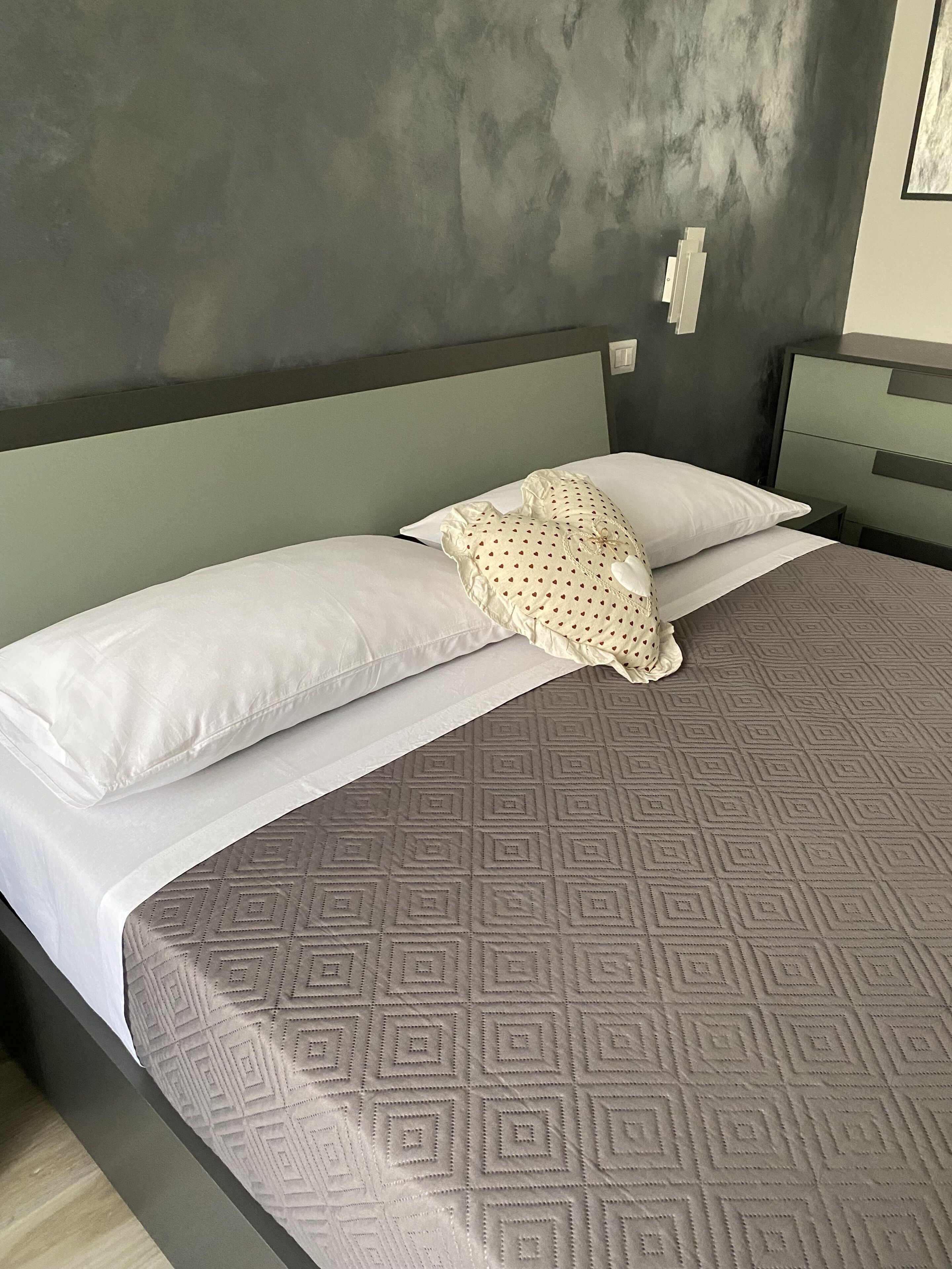 Een net opgemaakt bed met een laken met patroon, twee kussens en een sierkussen.