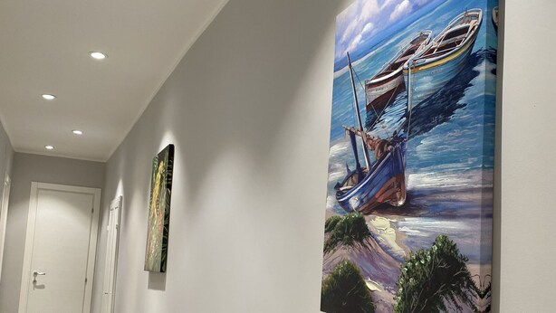 Un couloir orné d’un tableau représentant un bateau sur la mer, avec une porte au fond et un luminaire au plafond.