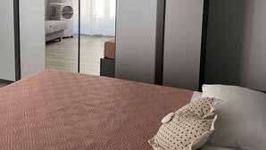 Une chambre moderne avec un grand lit, une armoire aux portes miroir et une vue sur une autre pièce.