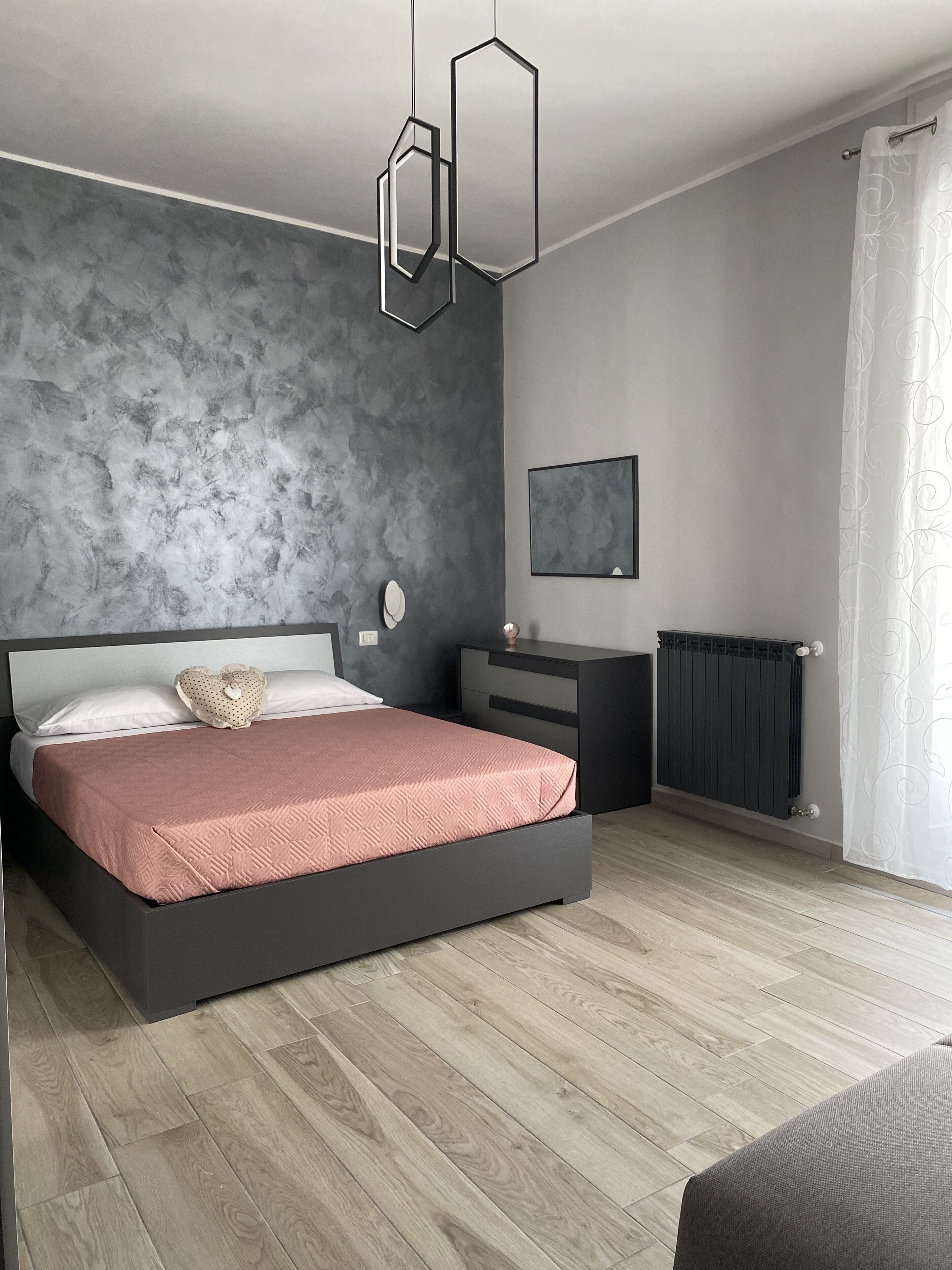 Un dormitorio moderno con una cama grande, una mesita de noche, un aparador, un radiador y una ventana con cortinas.