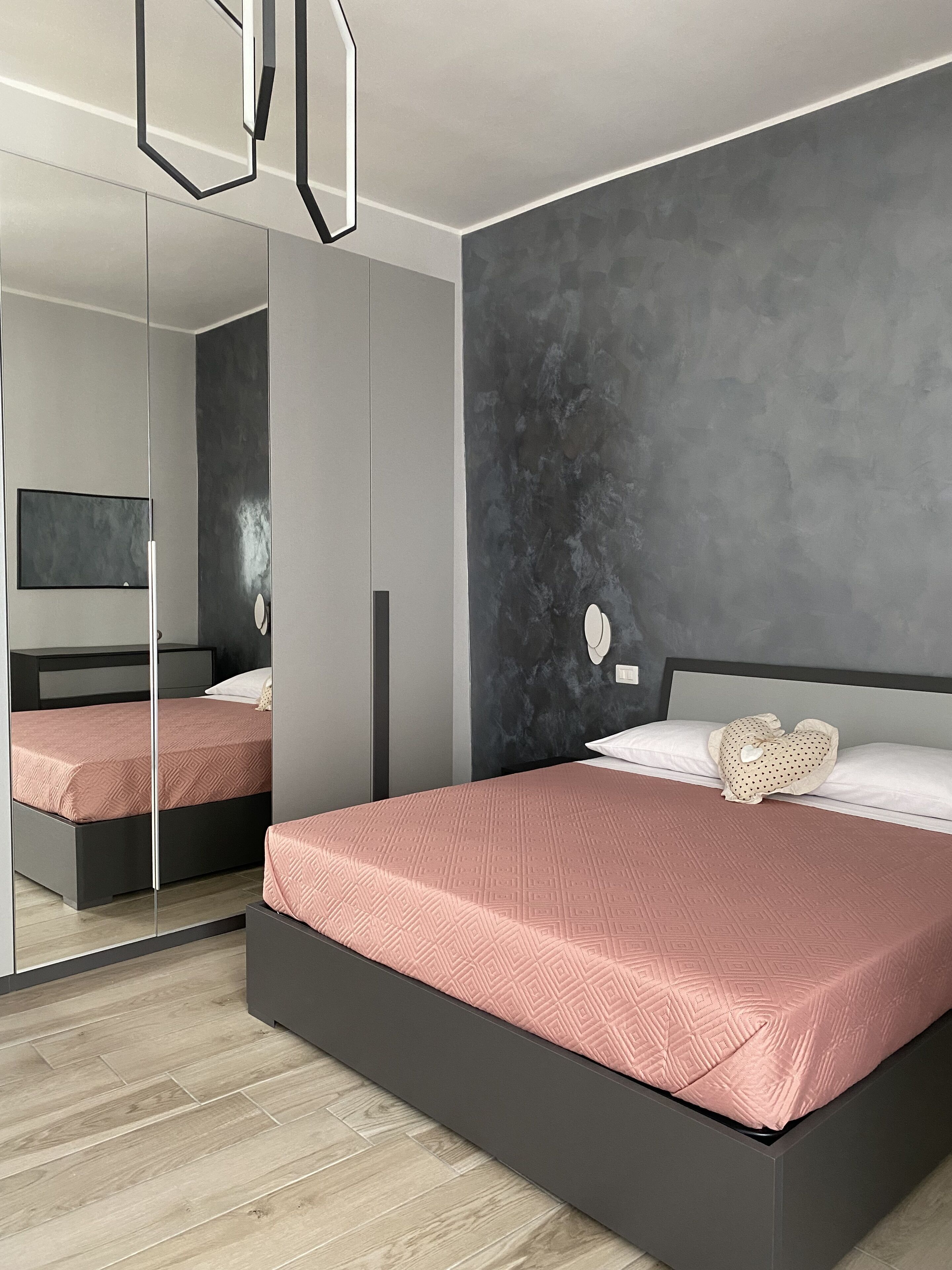 A modern bedroom with a large bed, a dark gray wall, and a mirror.