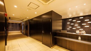A hotel reception area with a modern design, featuring a reception desk, a black wall with illuminated panels, and a tiled floor. - Floral Higashishinsaibashi Hotel (Osaka)