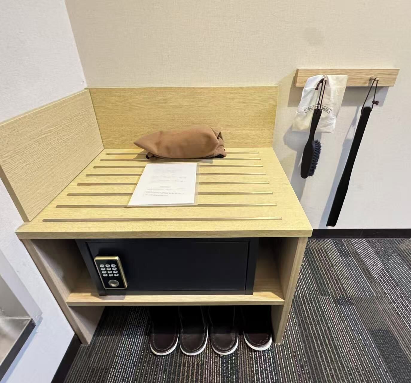 A hotel room with a wooden headboard, a pillow, a note, a shoe rack, and a wall-mounted phone.