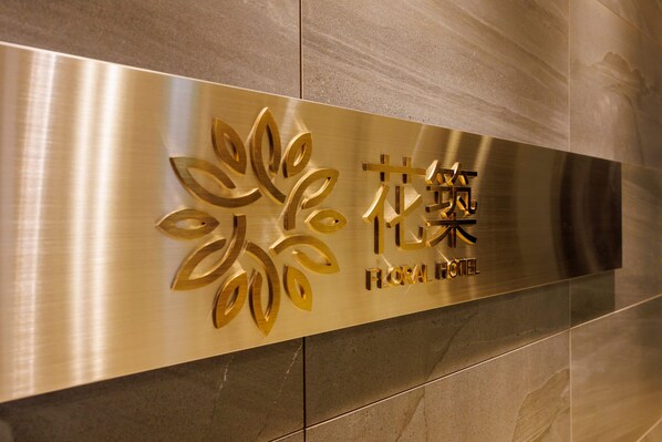 A metallic sign with stylized floral designs and the name "Floral Hotel" in both English and another script.