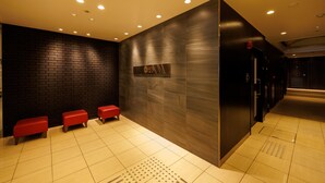 A modern lobby with a black brick wall, a marble wall, and a tiled floor. There are three red benches along the wall. - Floral Higashishinsaibashi Hotel (Osaka)