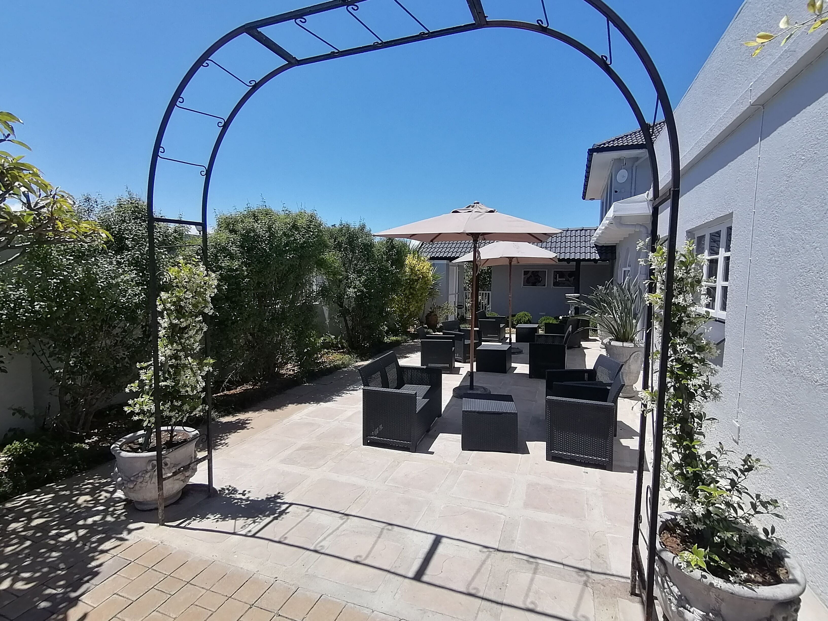 En udendørs terrasse med pergola, siddepladser og krukker med planter.