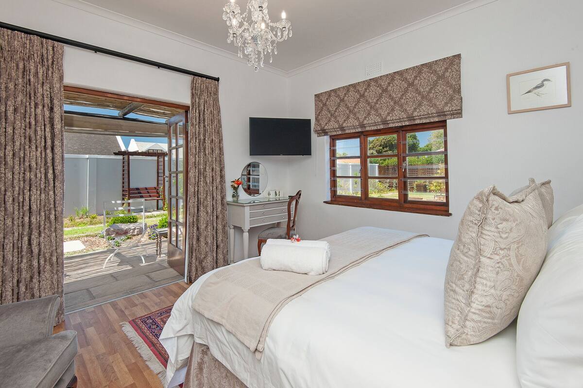 A bedroom with a large bed, a desk, a chair, a TV, and a window with a view of the outside.