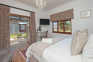 A bedroom with a large bed, a desk, a chair, a TV, and a window with a view of the outside. - Villa Venusta (Hermanus)