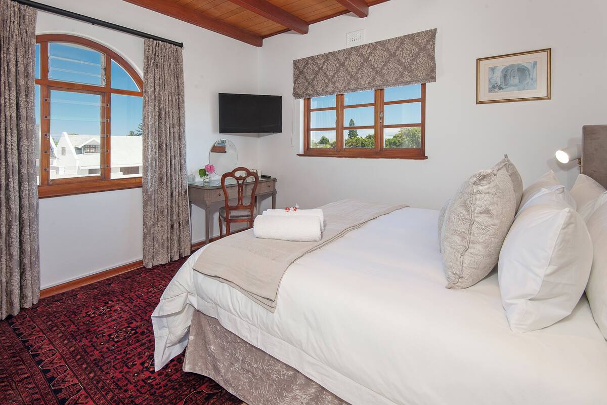 A hotel room with a large bed, a desk with a chair, a television, and a window with curtains.