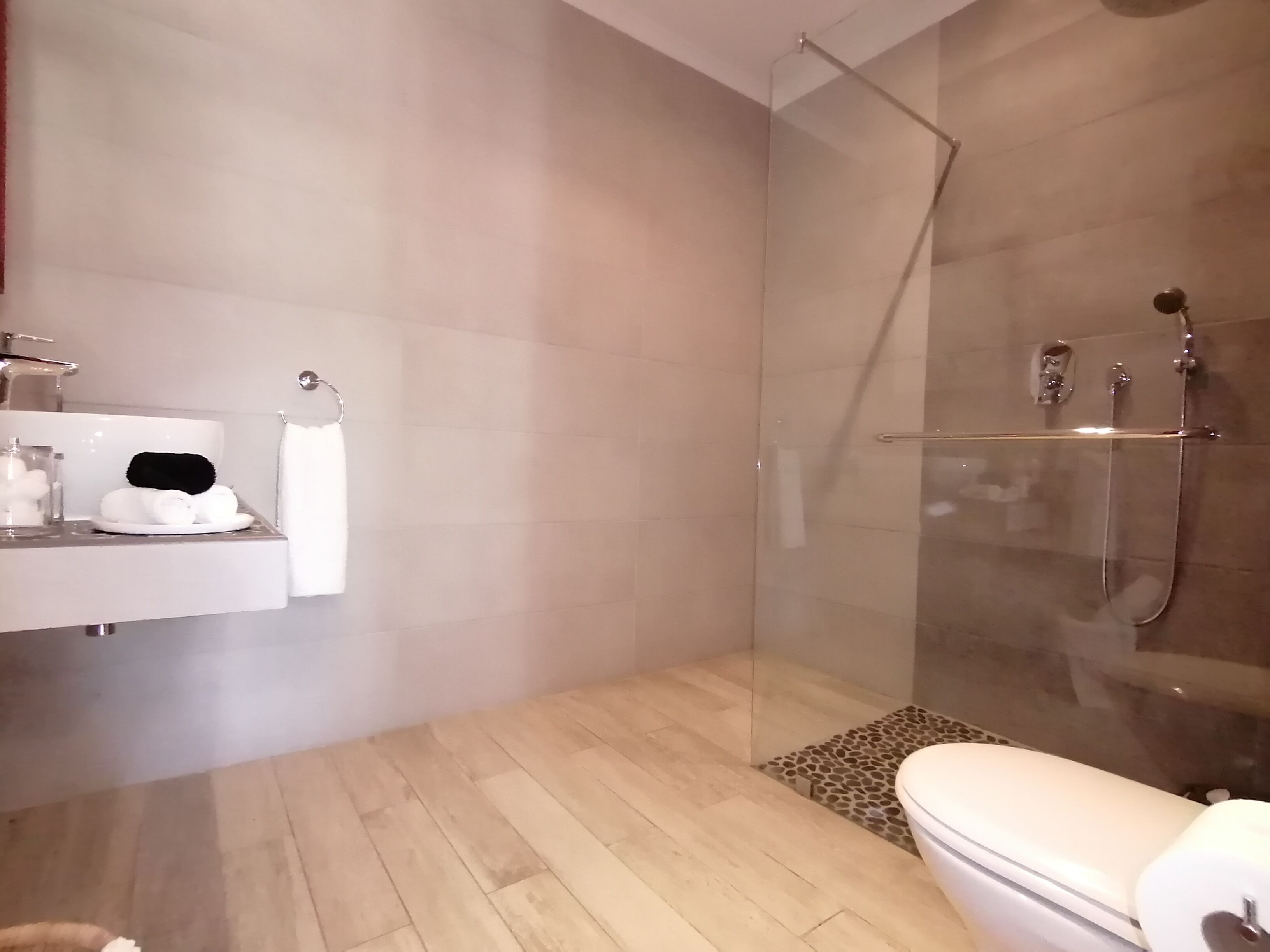 Une salle de bain moderne avec une douche à parois de verre, des toilettes blanches et un plancher en bois.