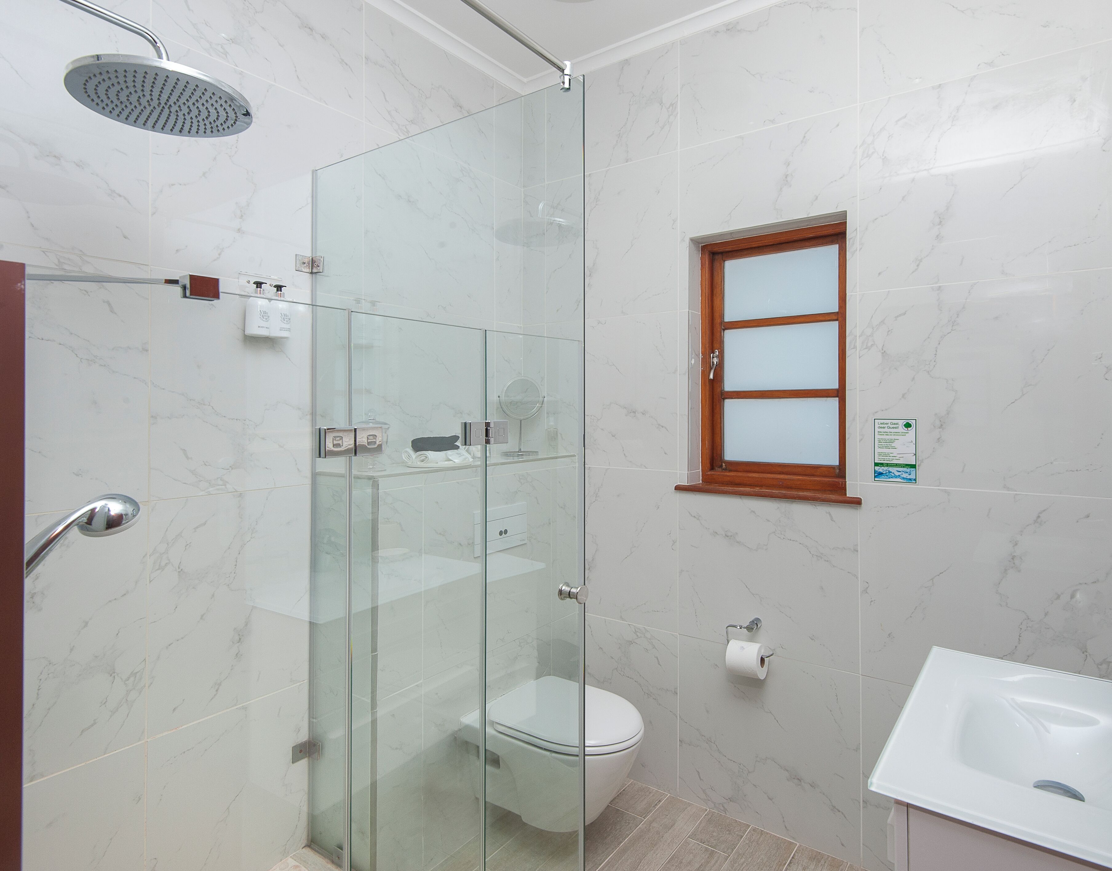 A modern bathroom with a glass-enclosed shower, a toilet, a sink, and a window with frosted glass panes.