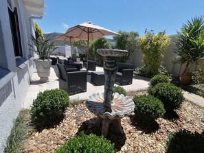 An outdoor patio with black wicker furniture, a stone fountain, and a large umbrella. - Villa Venusta (Hermanus)