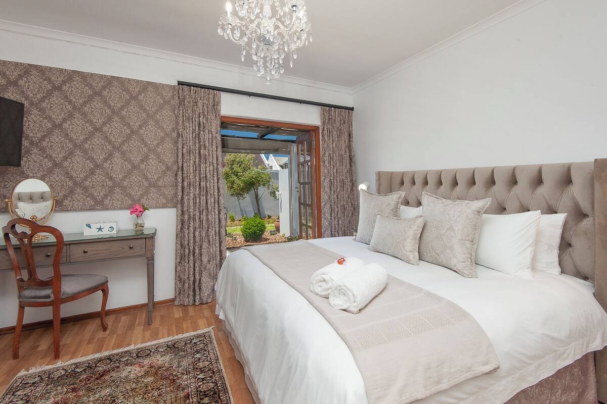 A bedroom with a large bed, a desk, a chair, and a view through an open door.